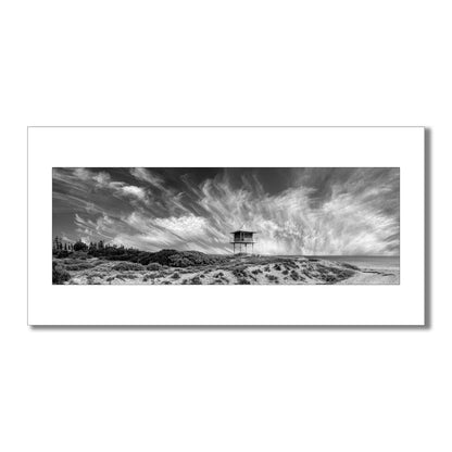 Escape to the coast with this breathtaking black and white panorama  art print of Semaphore Beach, Australia. Featuring a historic lookout tower and awe-inspiring clouds, this limited-edition print is a must-have for any art lover or traveller