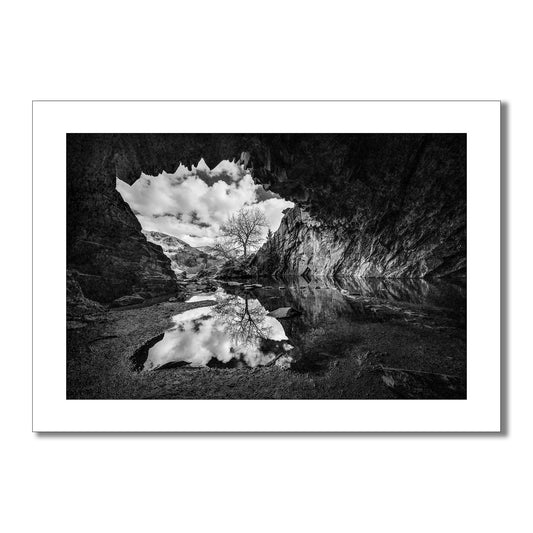Monochrome art print of the Witcher Cave from The Witcher series. Jagged rocks frame the entrance and a lone tree reflection in the pool of water in the cave.